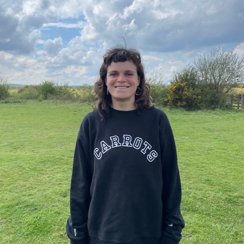 a dark haired white woman in a black sweatshirt against a natural background with an open field.