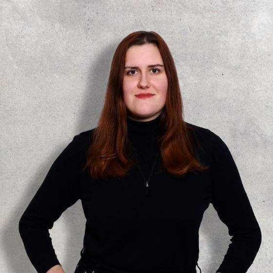 a dark haired white woman in a black turtleneck, against a marble background.